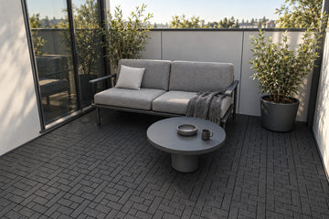 Black interlocking composite deck tiles in a sheltered terrace; AI installation visualization guided by the product’s 3D tile model.